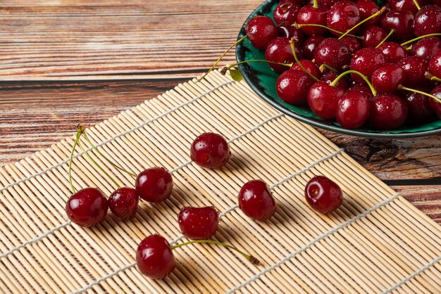 Red cherries with green stems in a decorative plate and on the mat