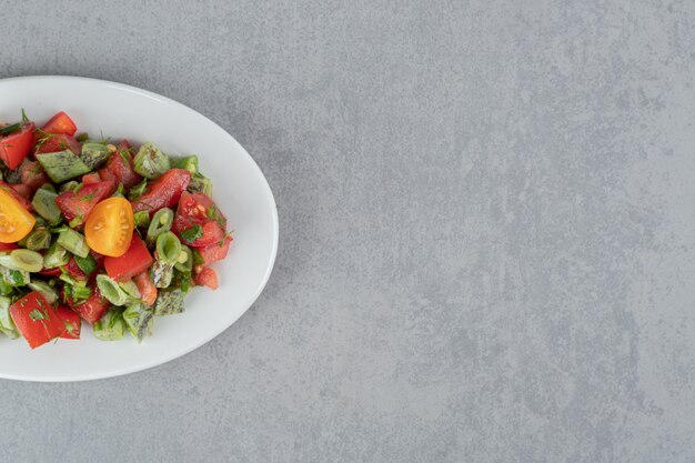 Салат из красных помидоров черри и фасоли в керамической тарелке
