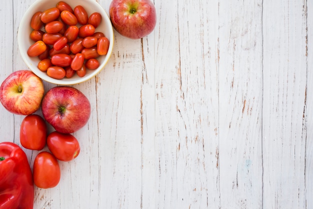 Red cherry tomatoes bowl; apple and bell pepper on white textured backdrop