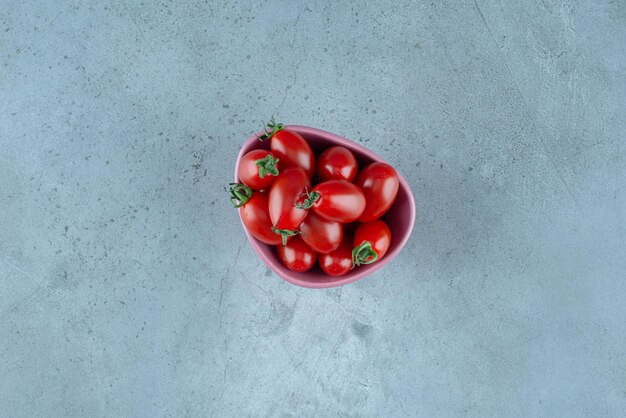 Red cherry tomatoes in a cup on blue.