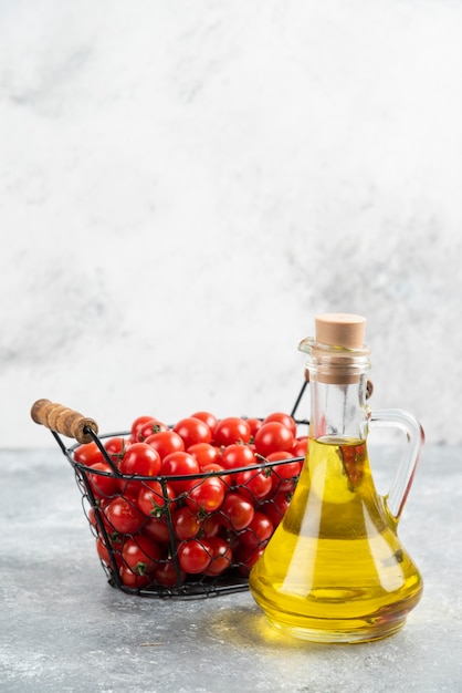 Red cherry tomatoes with a bottle of extra virgin olive oil on marble table.