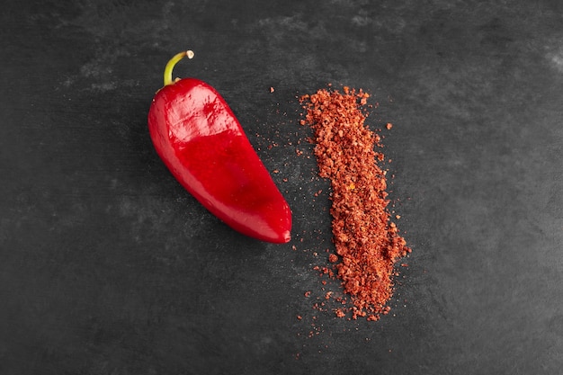 Red chili pepper with paprika on black surface.