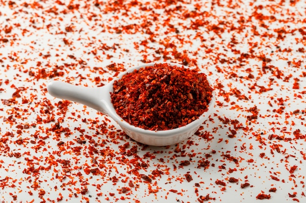 Порошок красного chili в белом ветроуловителе на белой и разбросанной предпосылке специи.