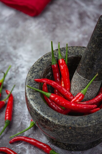 Red chillies are in a stone mortar on black surface.
