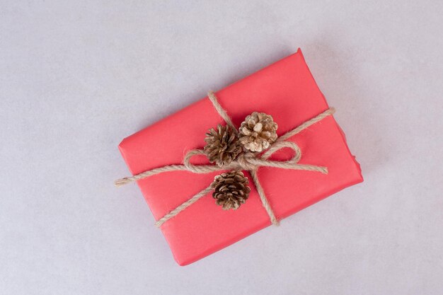 Red Christmas box with three pinecones on white table .