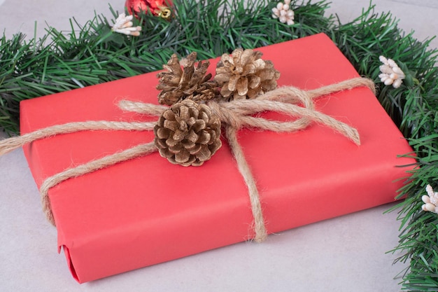 Red Christmas box with three pinecones on white table .