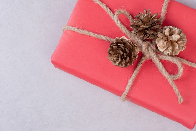 Red Christmas box with three pinecones on white .