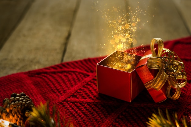 Red christmas gift box on red scraf with gold particles light magical on wooden desk.