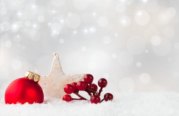 Red Christmas ornament and holly shrub berries, and a white star on a snowy surface