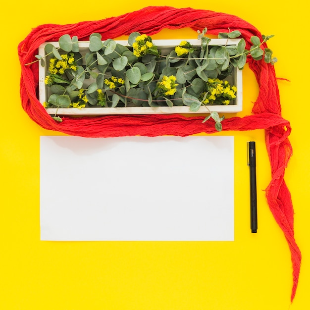 Free photo red clothes around the wooden box; pen and blank white paper on yellow background