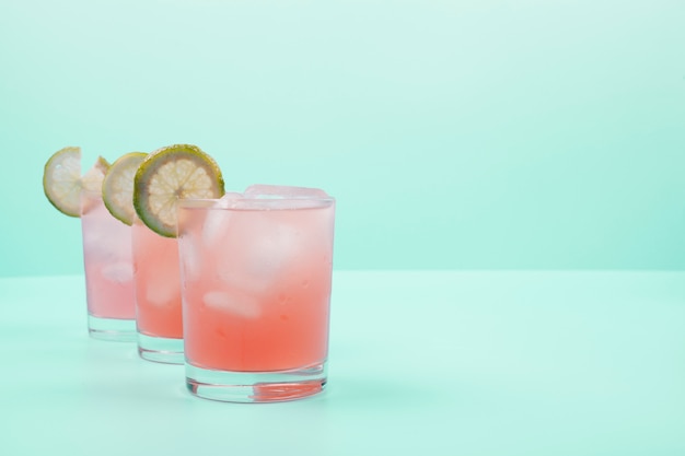 Free photo red cocktail glasses with lemon slices and ice cubes on mint background