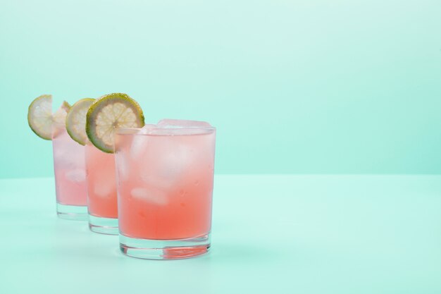 Red cocktail glasses with lemon slices and ice cubes on mint background