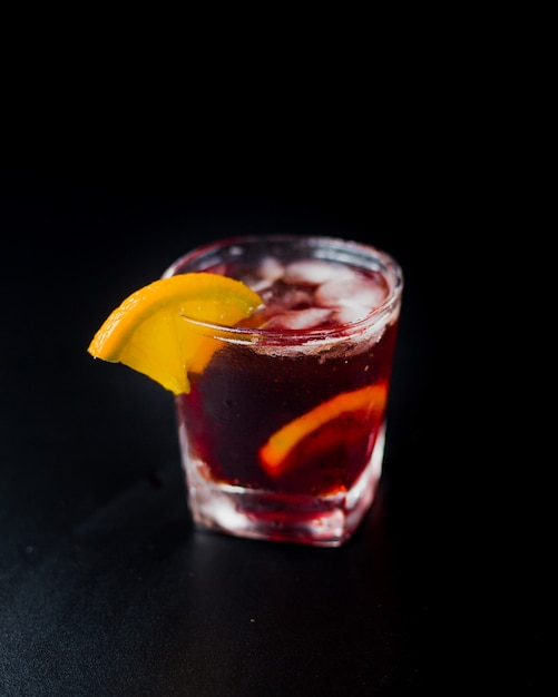 Red cocktail with ice cubes and lemon slices.