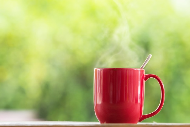 Red coffee mug on wooden tabletop against grunge green blur background