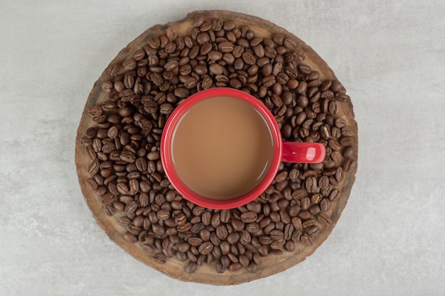 Red cup of coffee with coffee beans on wood piece