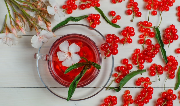 Foto gratuita bacche di ribes rosso con foglie, tè, fiori su legno.