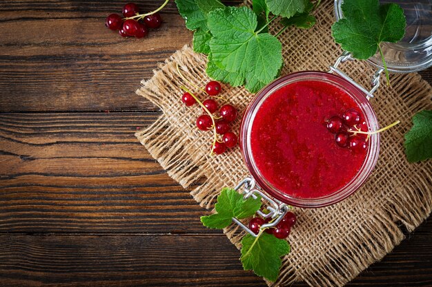 Red currant jam in a jar on a wooden surface. Tasty food.