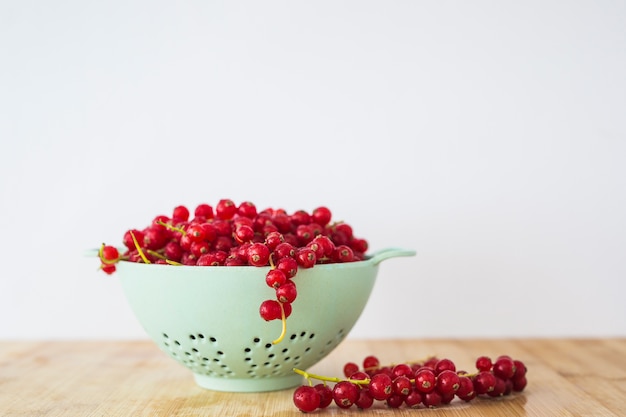 Free photo red currants in colander on wooden table against white background