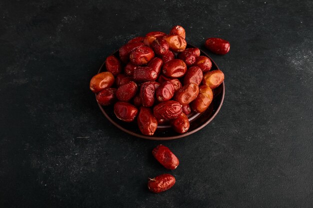 Red dates in a ceramic saucer on black surface. 