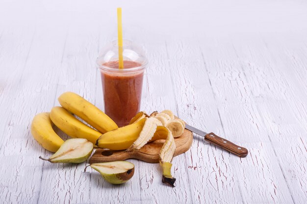 red detox coctail with bananas on chopping board lies on white table