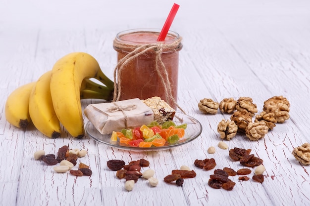 red detox coctail with bananas, walnut and candied fruits lies on white table