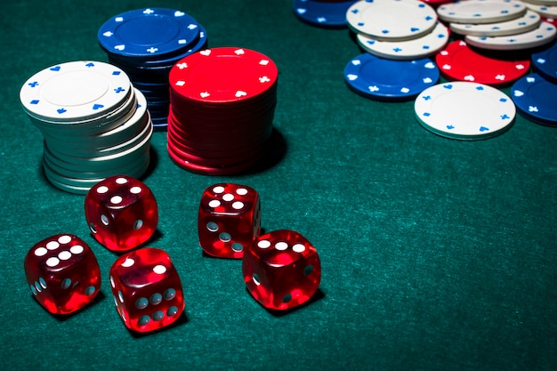 Red dices and stack of gambling chips on green poker table