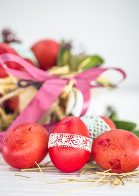 Red Easter eggs tied lace tape close-up, lying in an Easter basket with a bow, still life