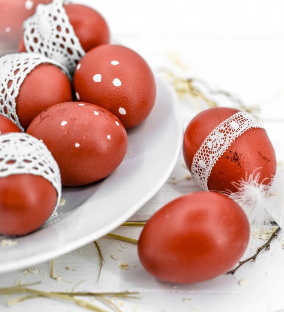 Red Easter eggs on a white plate and on white tied lace tape, close-up