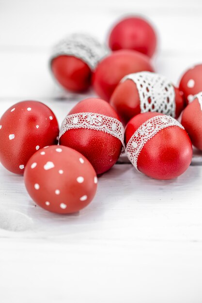 Red Easter eggs on white tied lace tape, close-up, lying on a white wood
