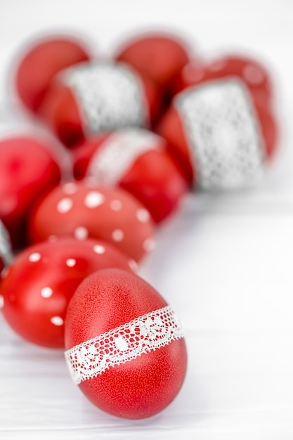 Red Easter eggs on white tied lace tape, close-up, lying on a white wood