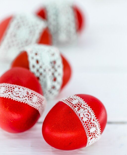 Red Easter eggs on a white tied with a lace ribbon, close-up, lying on a white wood