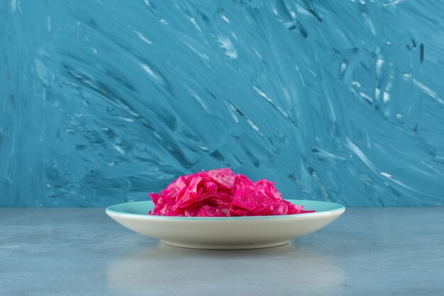 Red fermented sauerkraut on plate on the blue surface