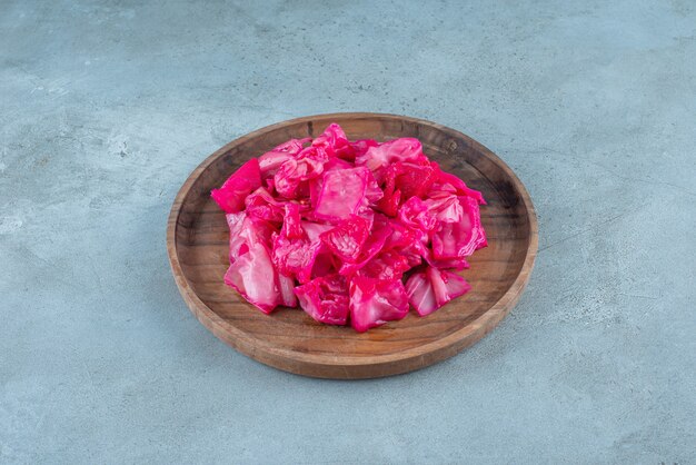 Red fermented sauerkraut on a wooden plate on the blue surface