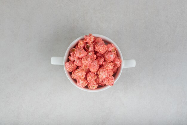 Red flavored popcorn in a bowl with handles on marble.