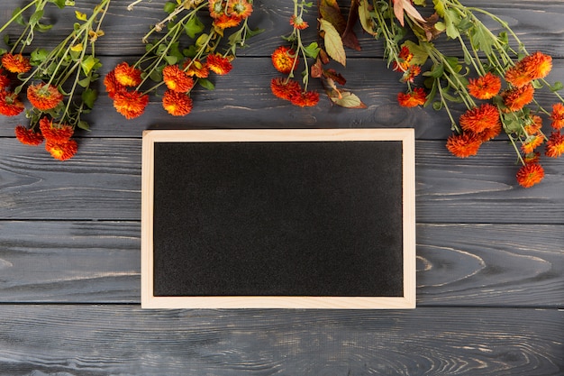 Free photo red flowers with blank chalkboard on wooden table