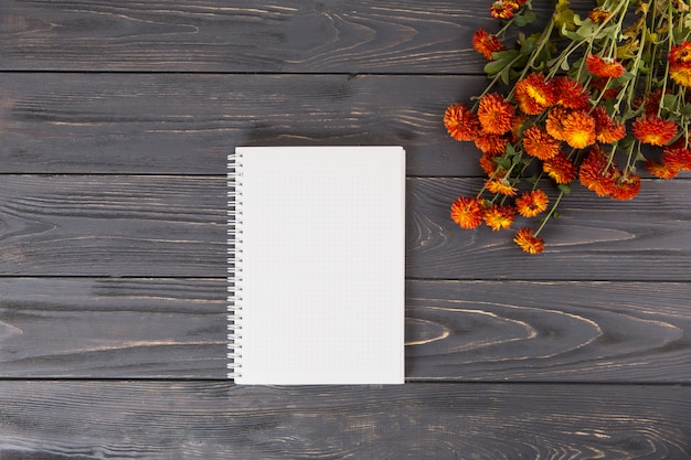 Free photo red flowers with blank notebook on wooden table