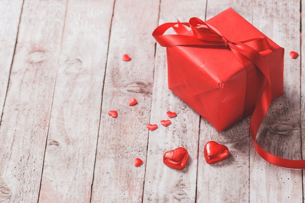 Red gift box on a wooden table with red hearts