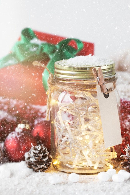 Red gift with green bow next to a glass jar with lights