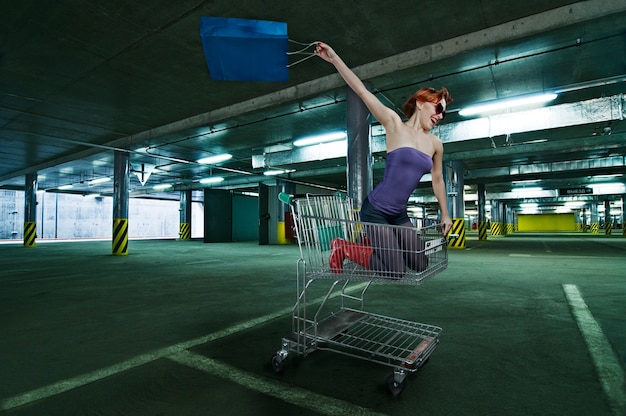 Free photo red girl riding shopping cart at the parking