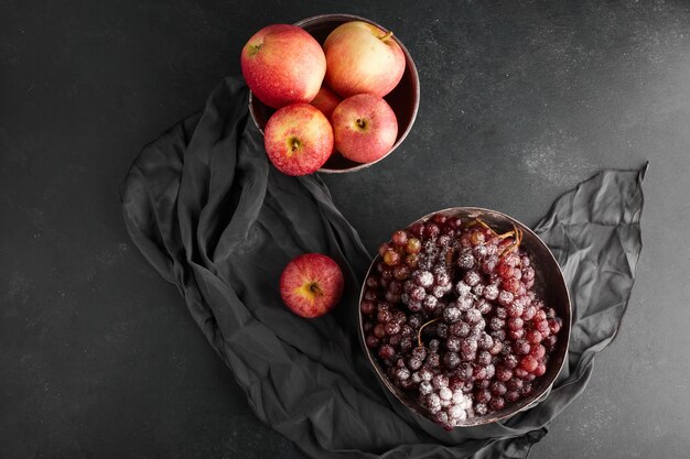 Грозди красного винограда и яблоки в металлических чашках, вид сверху.