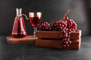 Бесплатное фото Грозди красного винограда в деревянном подносе с бокалом вина на черном.