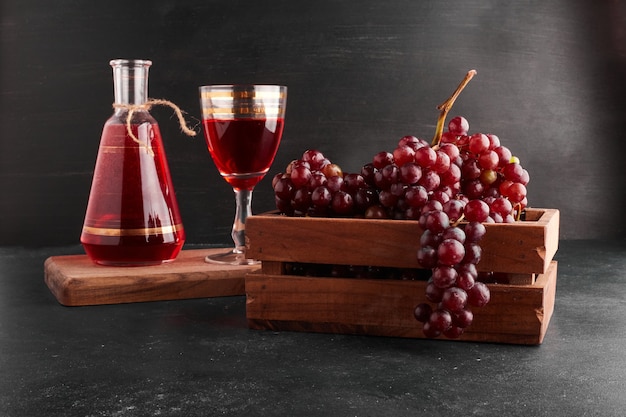 Red grape bunches in a wooden tray with a glass of wine on black. 