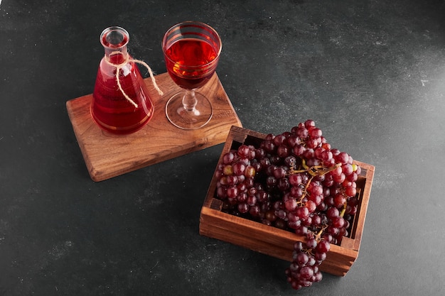 Red grape bunches in a wooden tray with a glass of wine. 