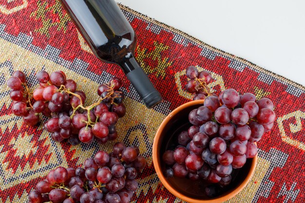 白と伝統的な敷物の上にフラットワインとボウルに赤ブドウを置く