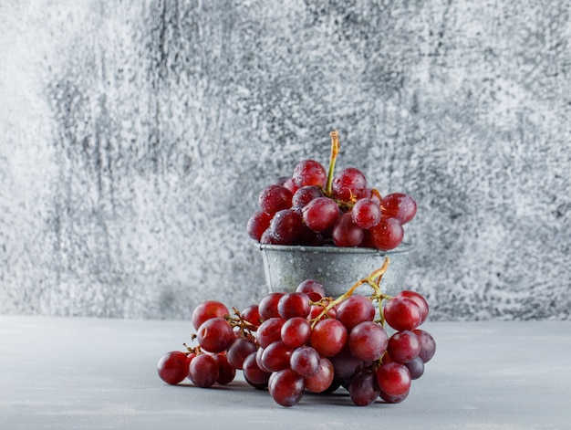 Red grapes in a mini bucket on plaster and grungy.