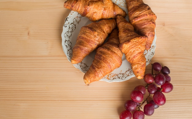 Red grapes near the baked croissant on plate over wooden background
