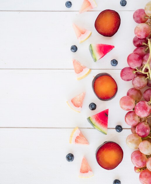 Красный виноград; треугольные ломтики арбуза; грейпфруты и черника на деревянный стол
