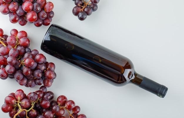 Free photo red grapes with wine bottle flat lay on a white