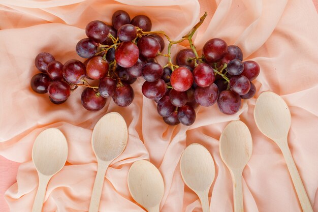Red grapes with wooden spoons flat lay on a pink textile