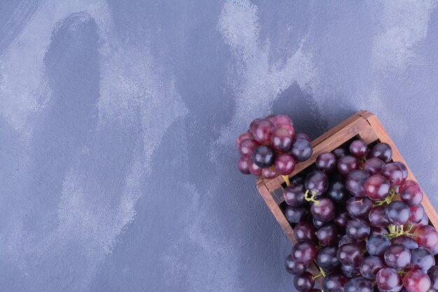 Red grapes in a wooden tray on blue surface